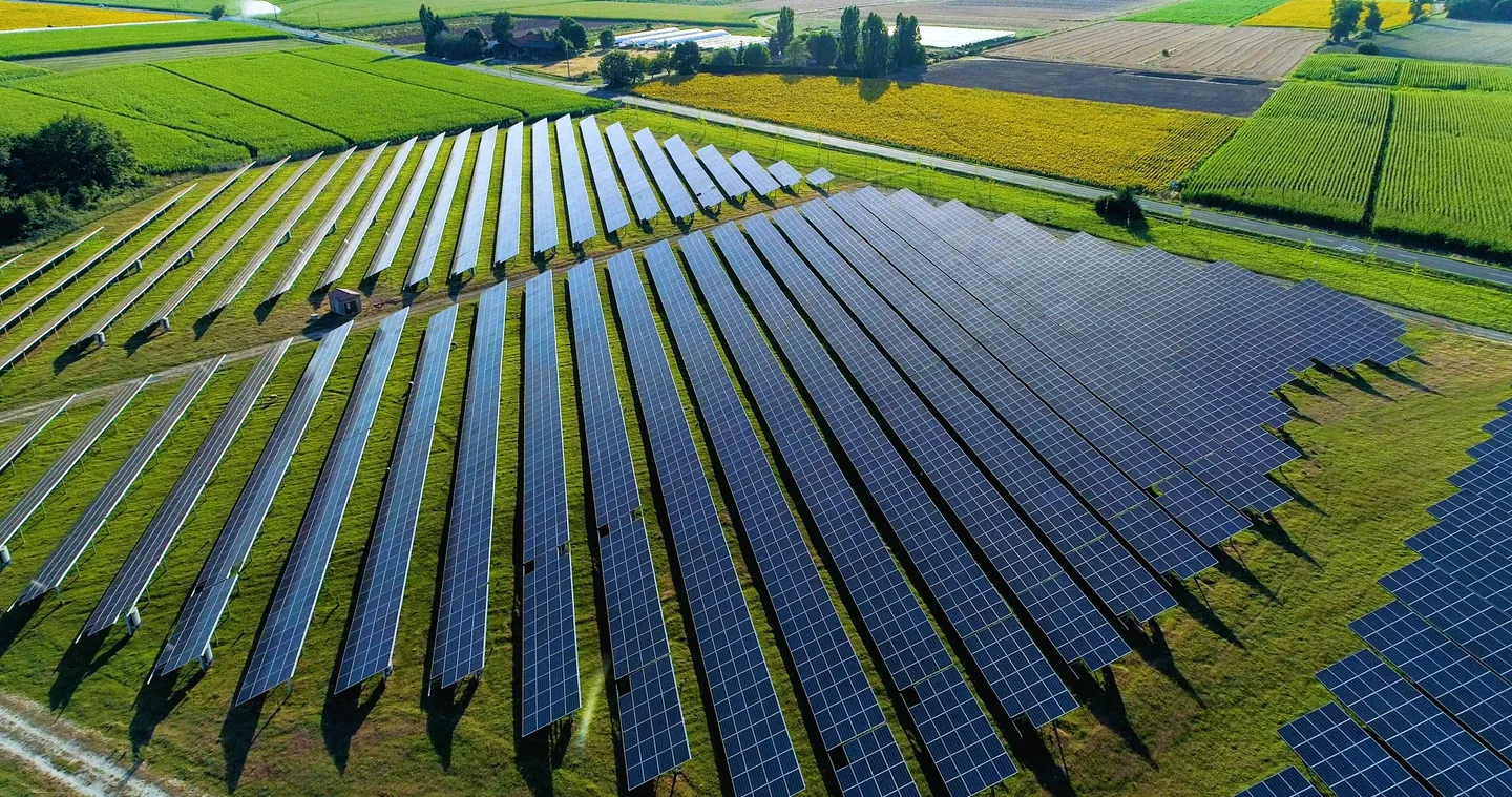 Aerial view of ground-mounted solar panels surrounded by green fields